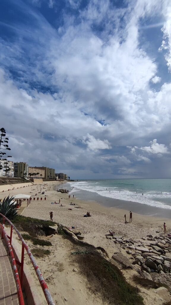 A long Cadiz beach under big dramatic clouds with turquoise Atlantic surf