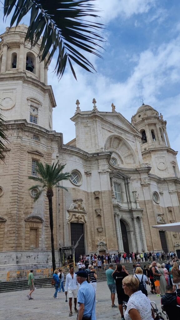 The baroque facade of Cadiz Cathedral framed by a palm frond