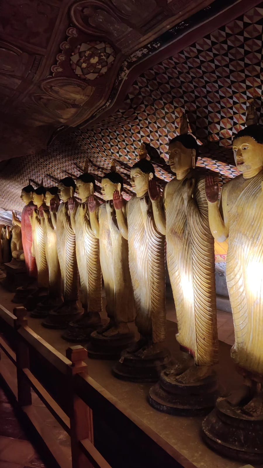 Row of golden standing Buddha statues in warm light inside the Dambulla cave temple