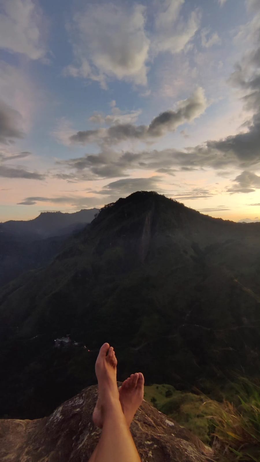 Bare feet on a cliff edge looking toward Ella Rock at dusk