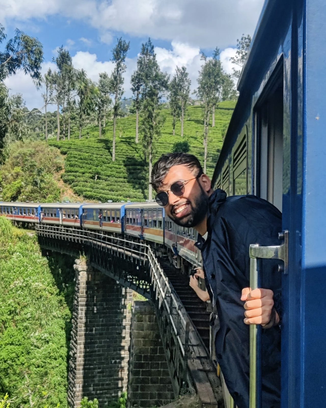 Leaning out of the blue train door over tea plantation hills on the way to Ella