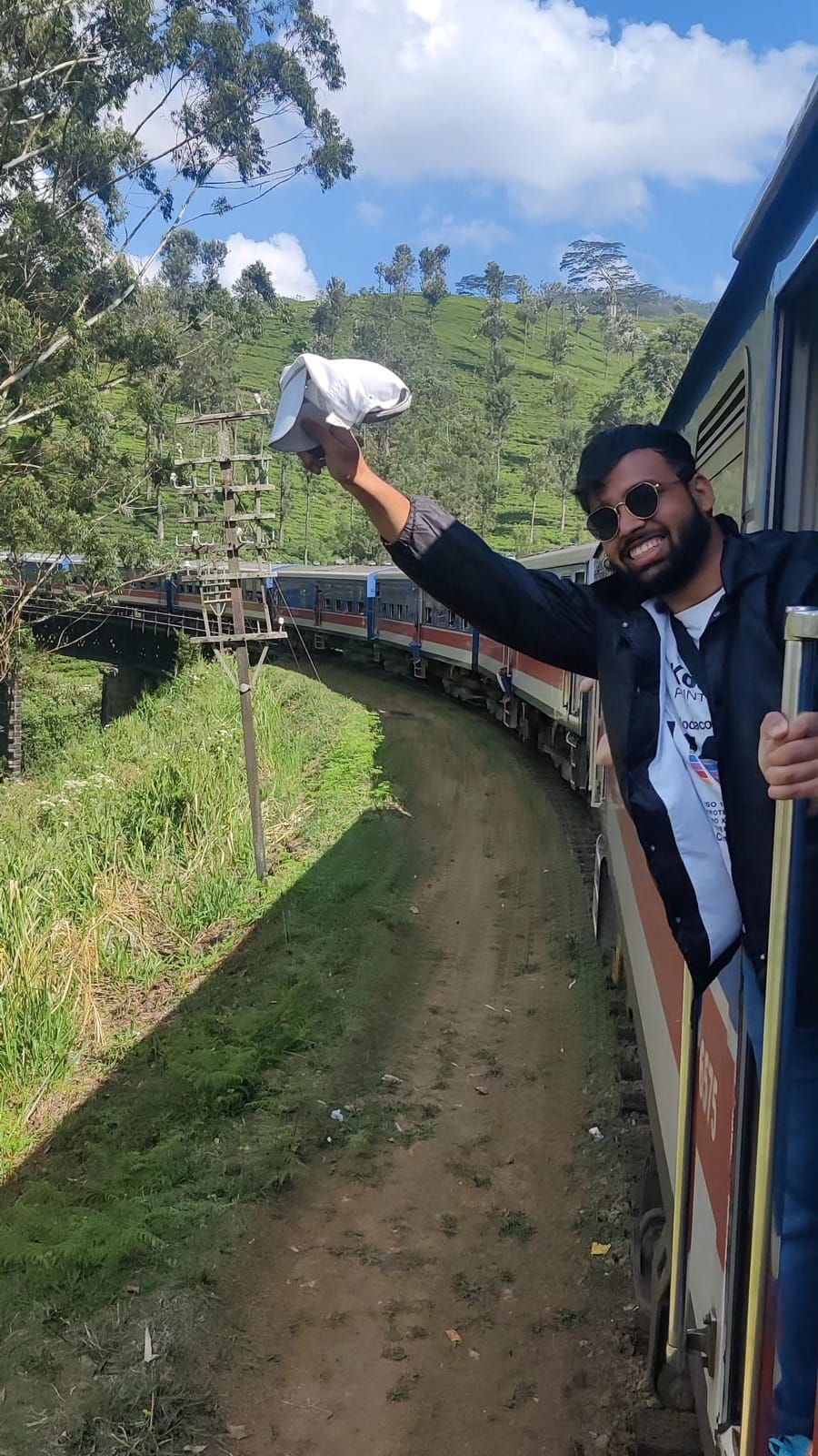 Waving a cap out of the train door as the blue train snakes around a tea plantation bend