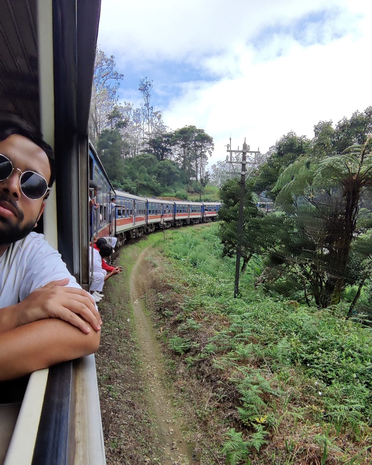 Leaning out of the train window in sunglasses as the long blue train curves along the hillside