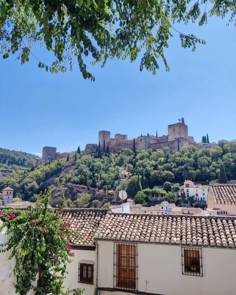 The Alhambra peeking over tiled Albaicin rooftops framed by bougainvillea, Granada