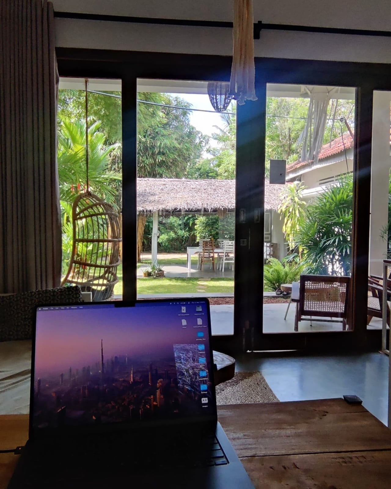 Laptop on a desk facing a tropical garden and thatched cabana while working remotely from Hiriketiya, Sri Lanka