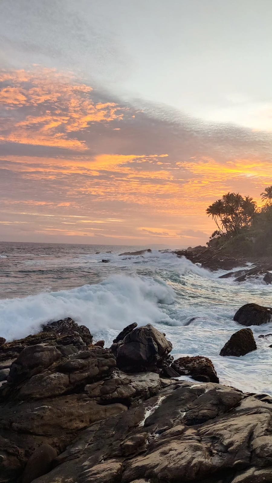 Waves crashing on the rocky coastline under a fiery sunset near Hiriketiya