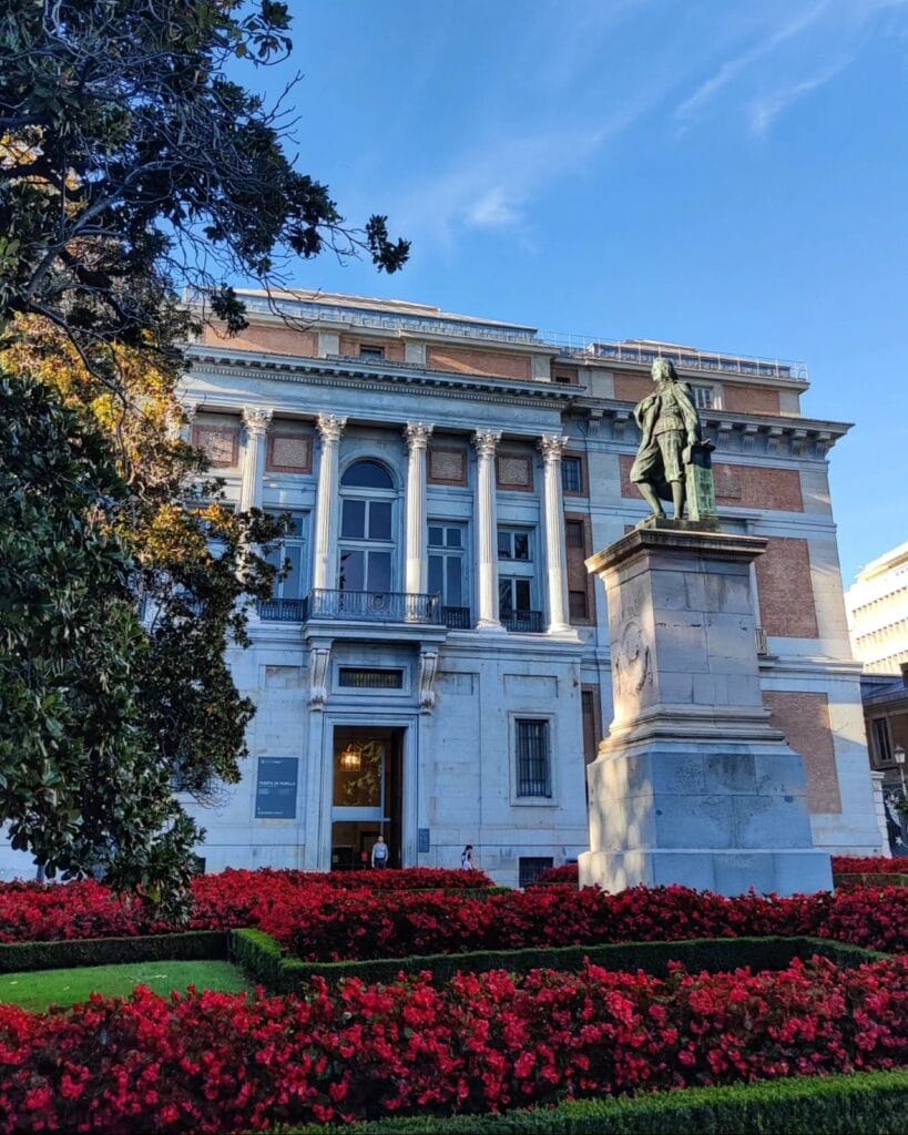Neoclassical facade and bronze statue of the Museo del Prado with red flowers, Madrid