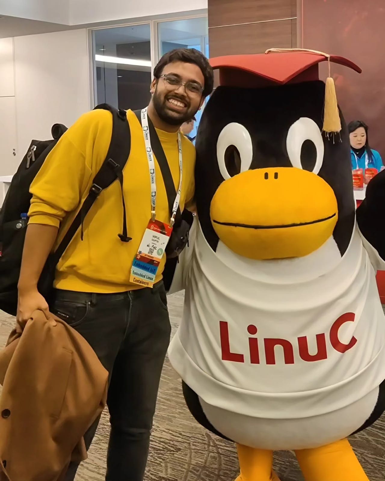 The author posing with the LinuC penguin mascot in a graduation cap at Open Source Summit Japan