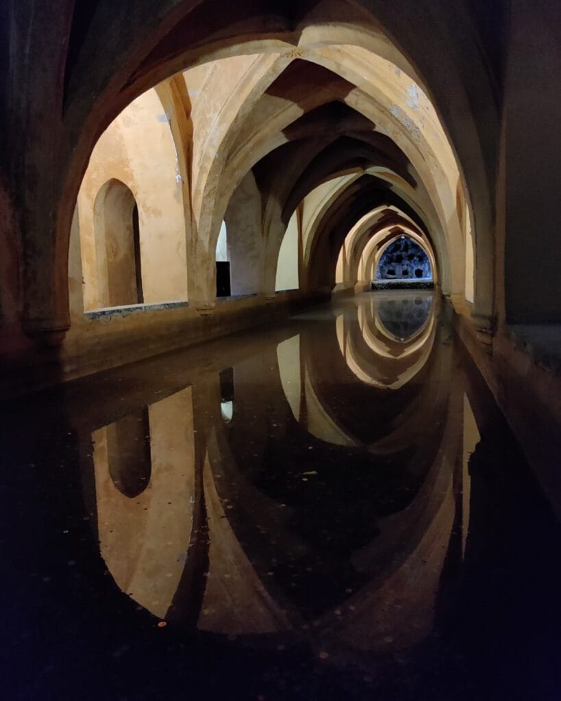 Vaulted Gothic arches reflected in the still water of the Banos de Dona Maria de Padilla, Real Alcazar of Seville