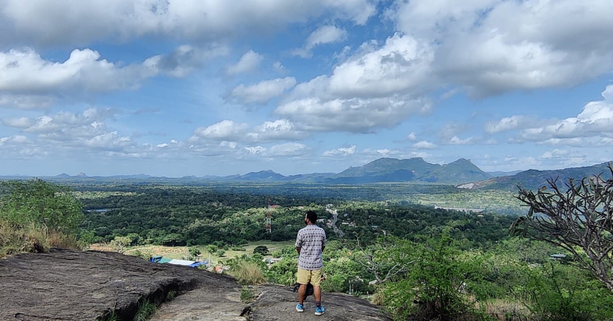 Traveller overlooking the green plains and distant mountains from the Dambulla rock summit in Sri Lanka