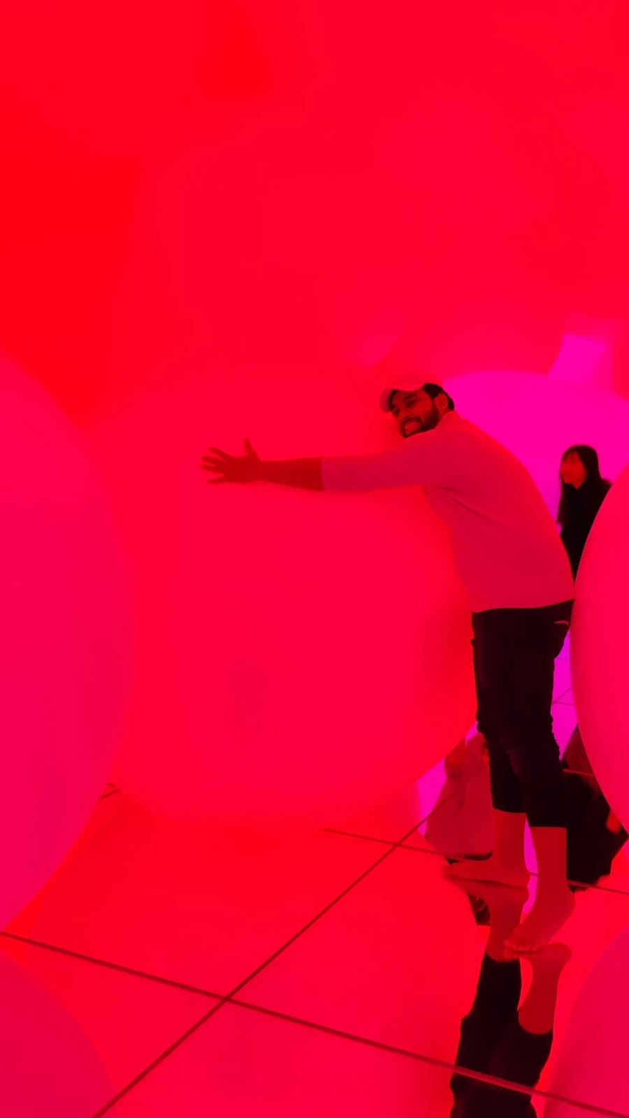 The author stretching both arms across a huge balloon in the red-lit sphere room at teamLab Planets