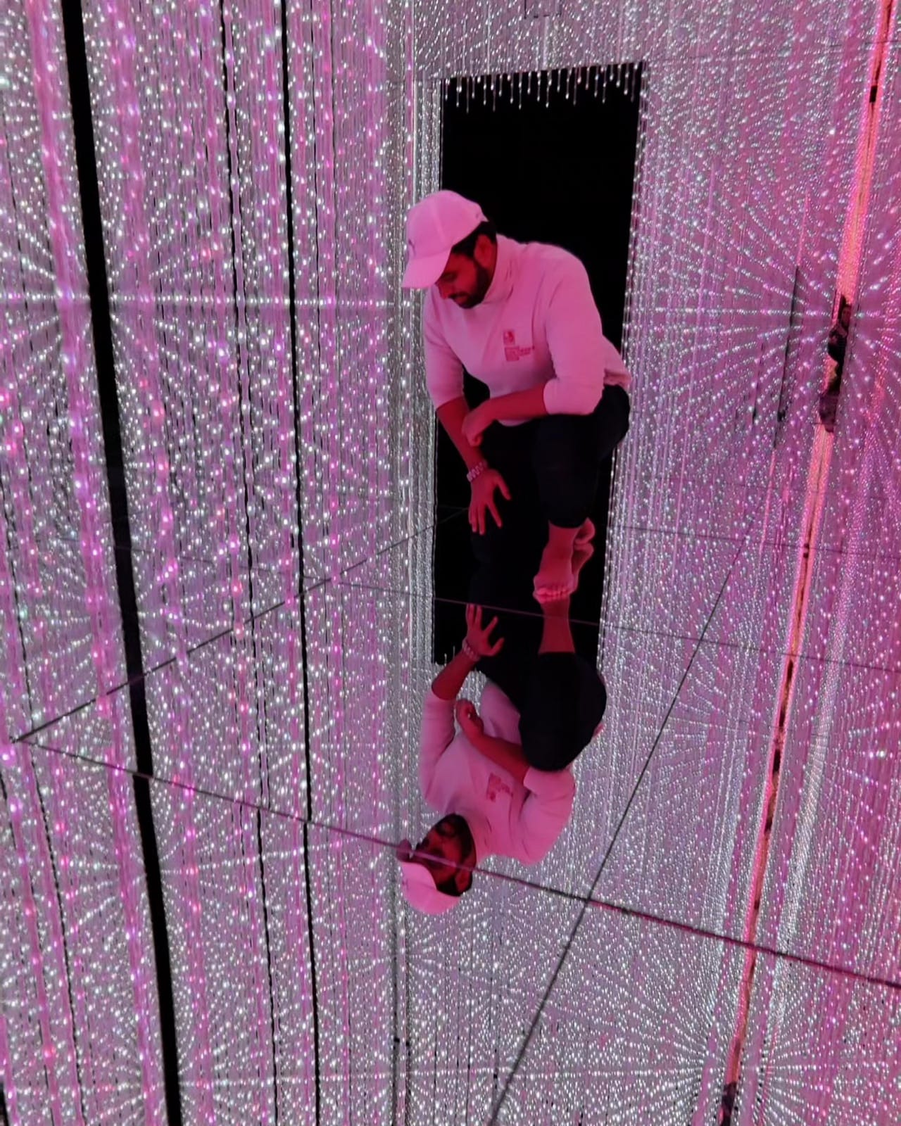 The author crouching in a pink LED corridor of the Infinite Crystal Universe at teamLab Planets, reflected in the mirror floor