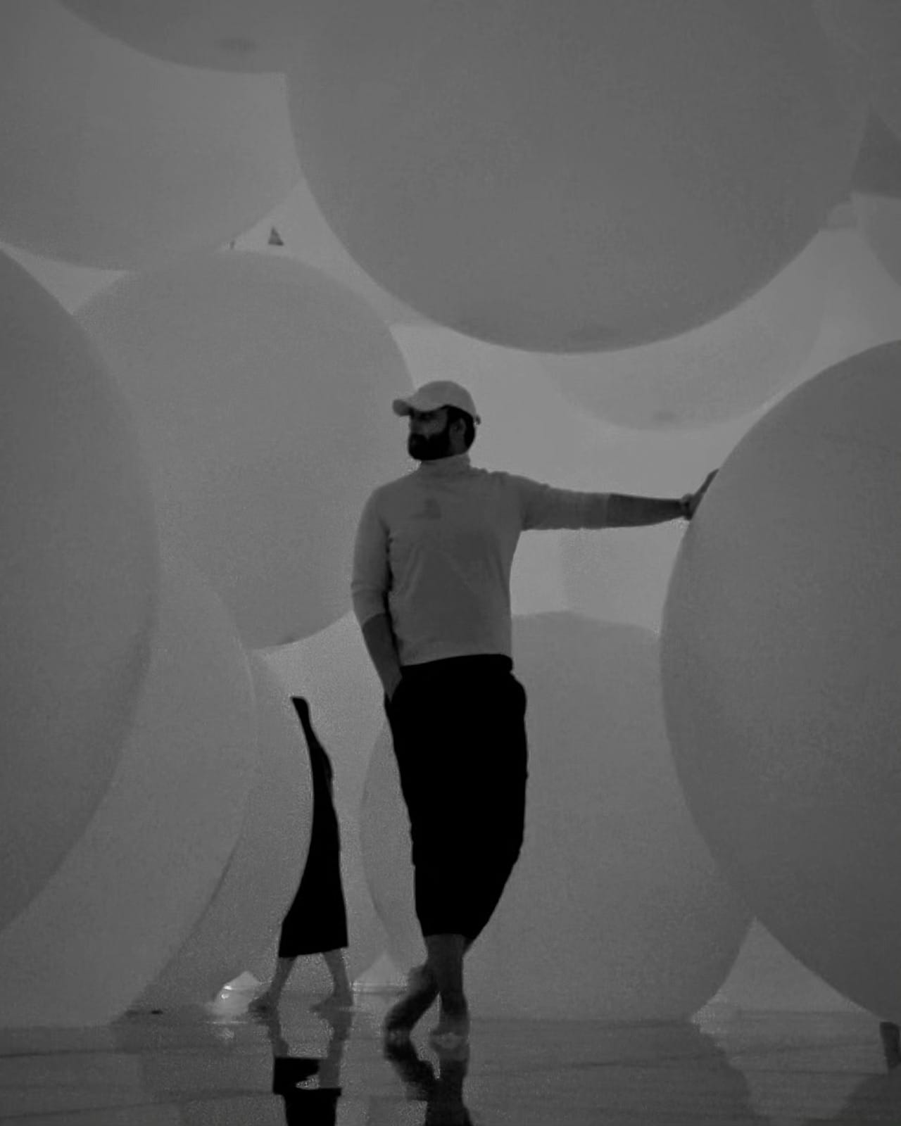 The author leaning against giant floating spheres in the balloon room at teamLab Planets, rendered in monochrome