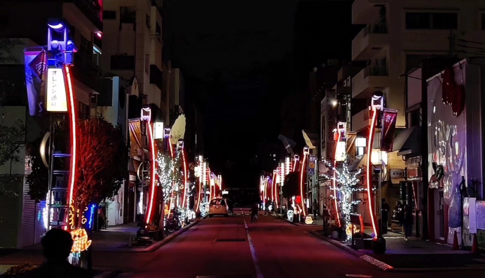 Orange-dori street in Asakusa at night with curved red neon poles and trees wrapped in winter illuminations