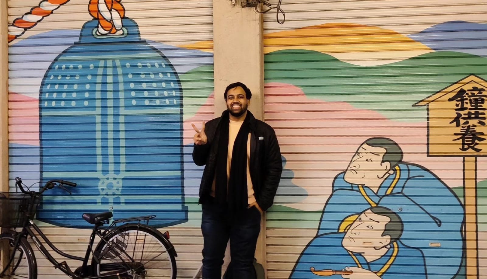 The author flashing a peace sign in front of a painted ukiyo-e shutter mural on an Asakusa backstreet