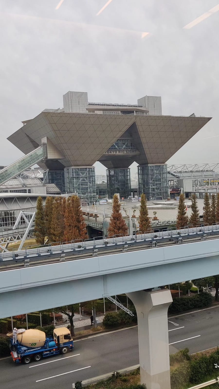 Tokyo Big Sight's inverted pyramid towers seen past the elevated Yurikamome line and autumn trees
