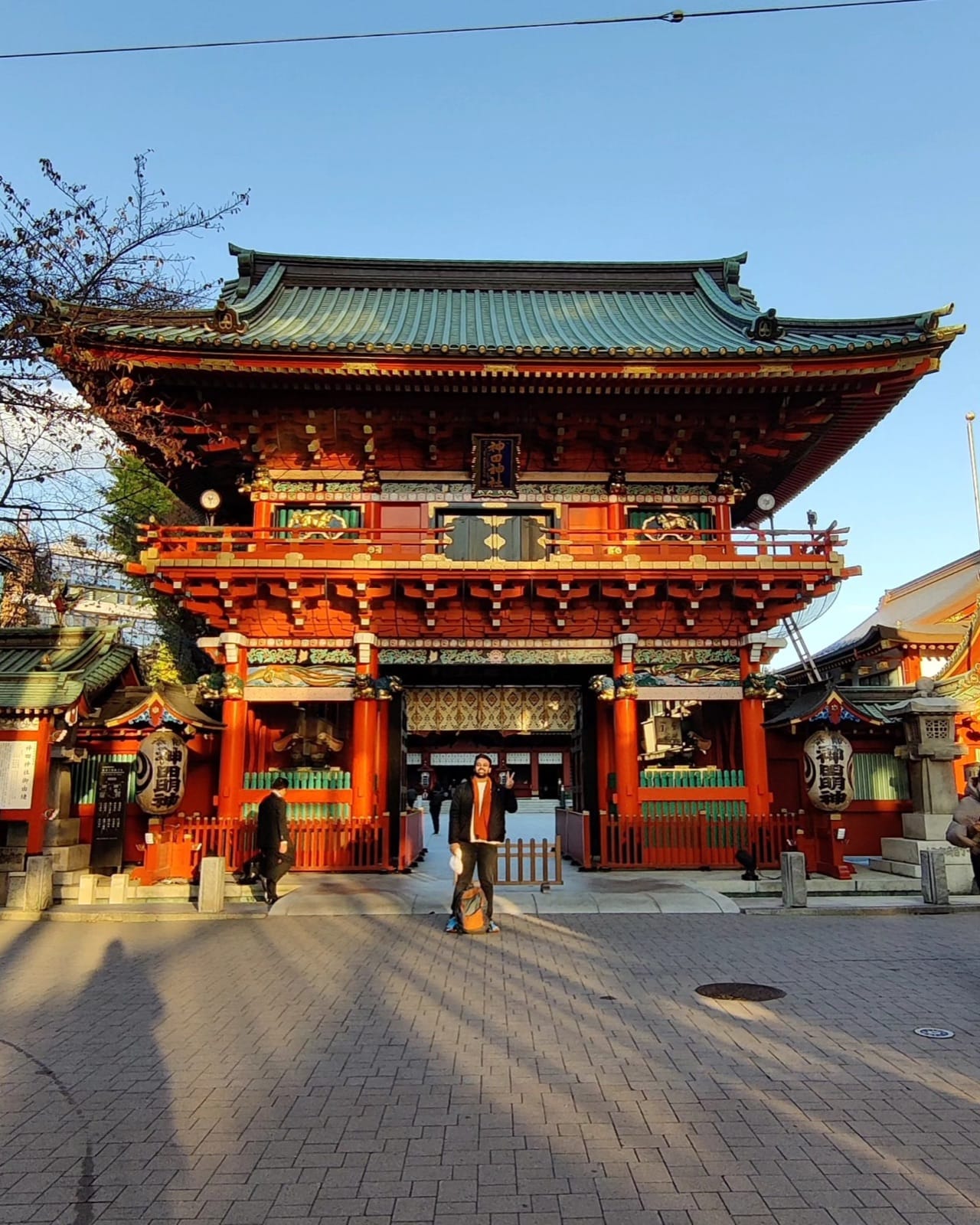 The author standing before the two-story vermilion Zuishin-mon gate of Kanda Myojin shrine in Tokyo