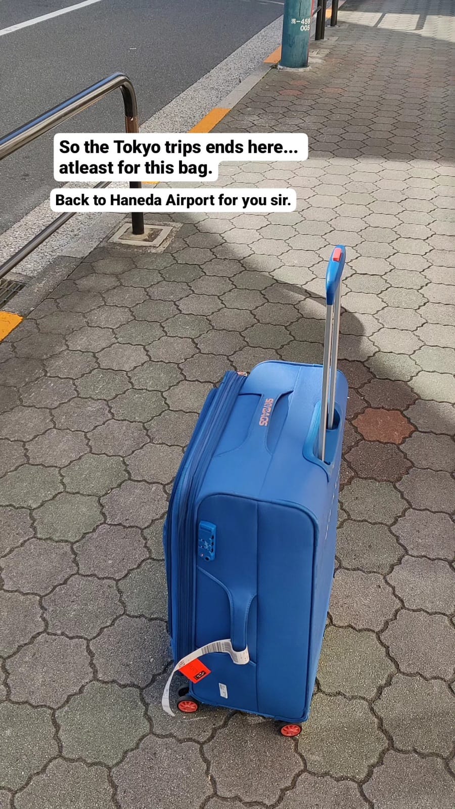 The stranger's blue suitcase standing on an Asakusa sidewalk before its trip back to Haneda Airport