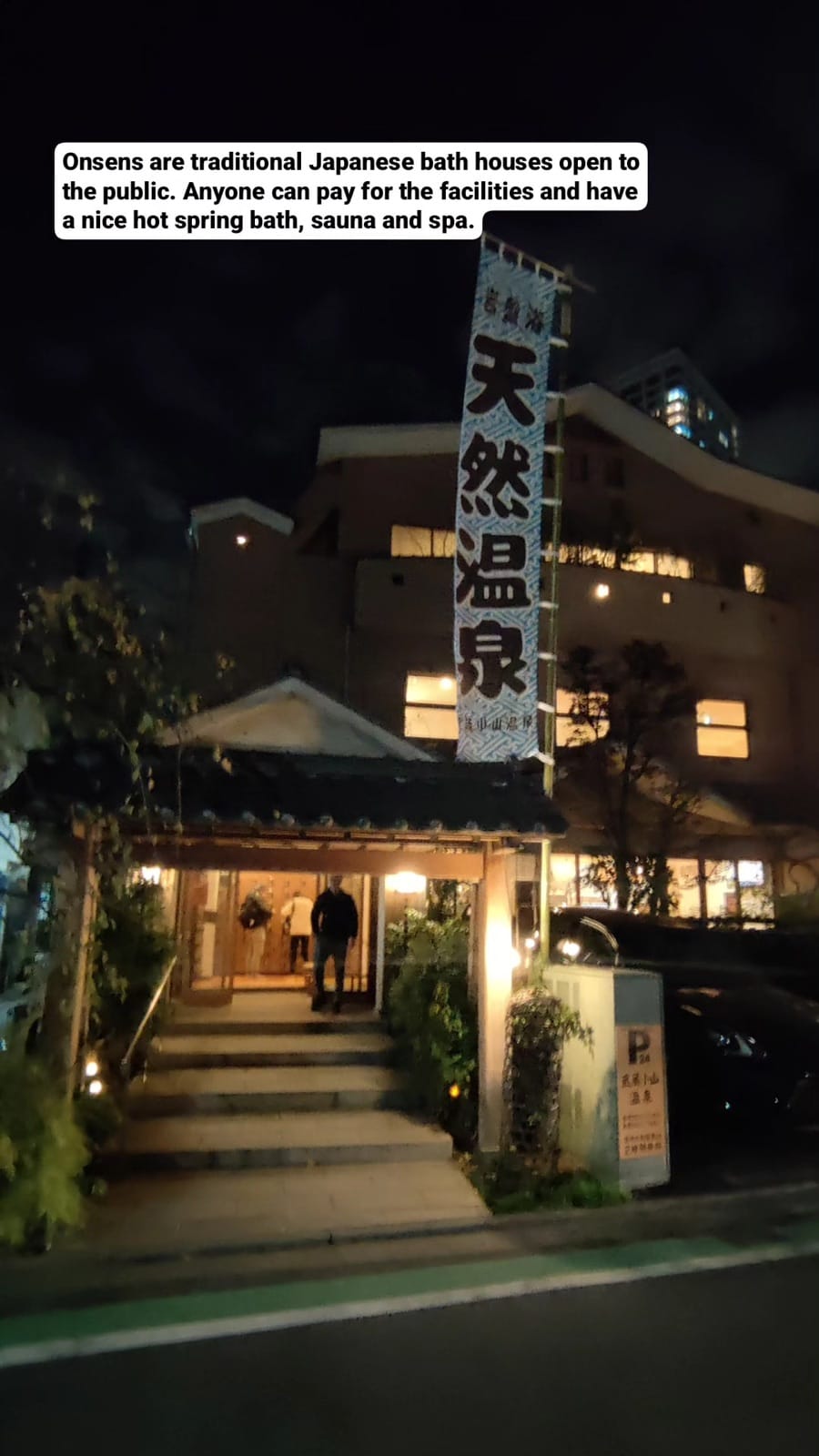 Night entrance of the Musashi-Koyama natural hot spring bathhouse with a vertical onsen banner over the steps