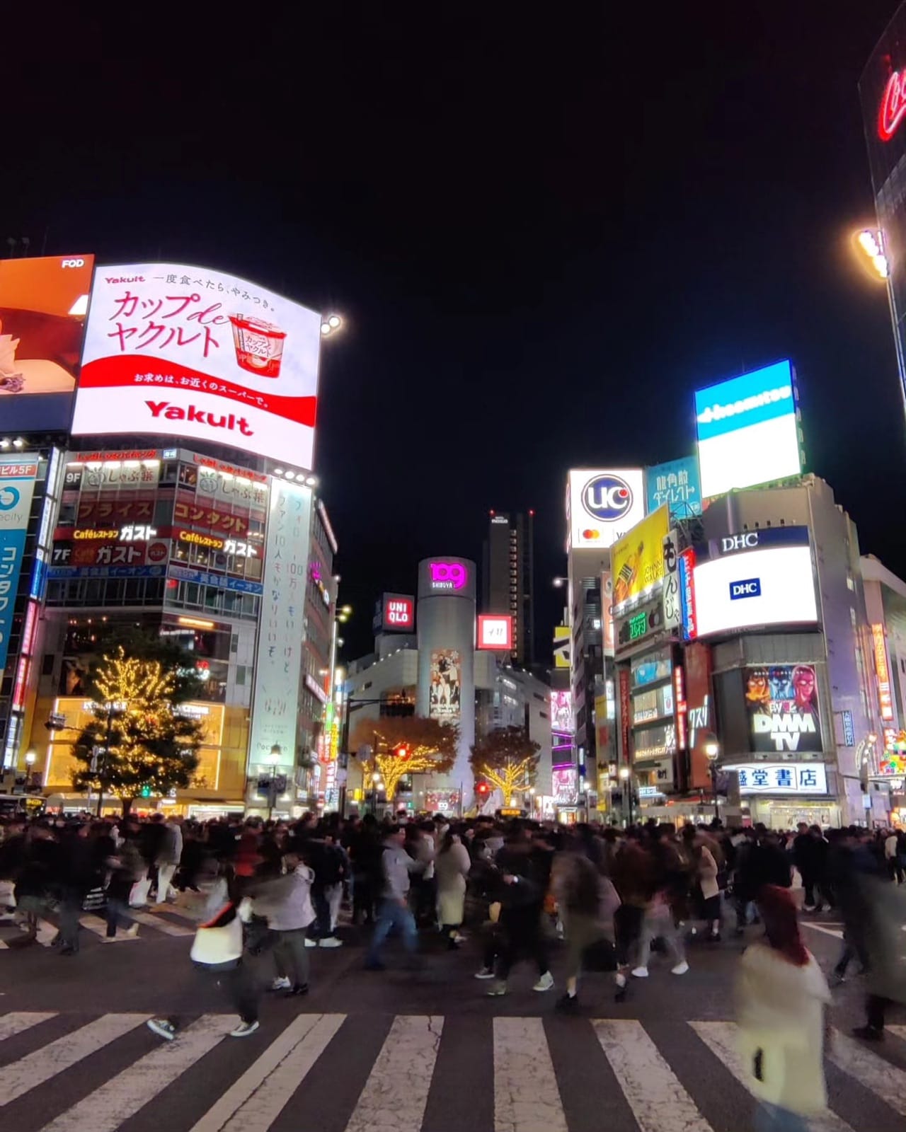 Crowds surging across Shibuya Scramble Crossing at night beneath glowing billboards in Tokyo