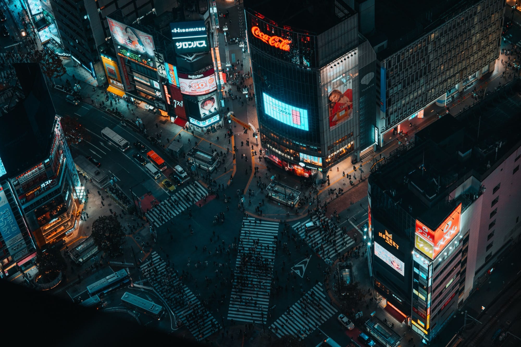 Crowds crossing the Shibuya Scramble Crossing at night under giant video billboards in Tokyo