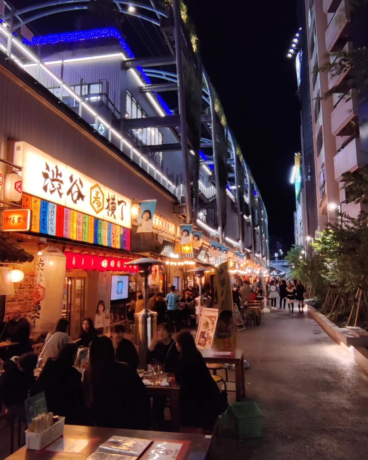 Diners at outdoor tables along the lantern-lined Shibuya Yokocho food alley at Miyashita Park