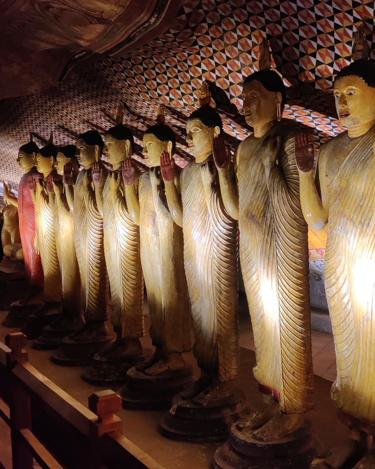 A row of standing Buddha statues glowing in lamplight inside the Dambulla cave temple