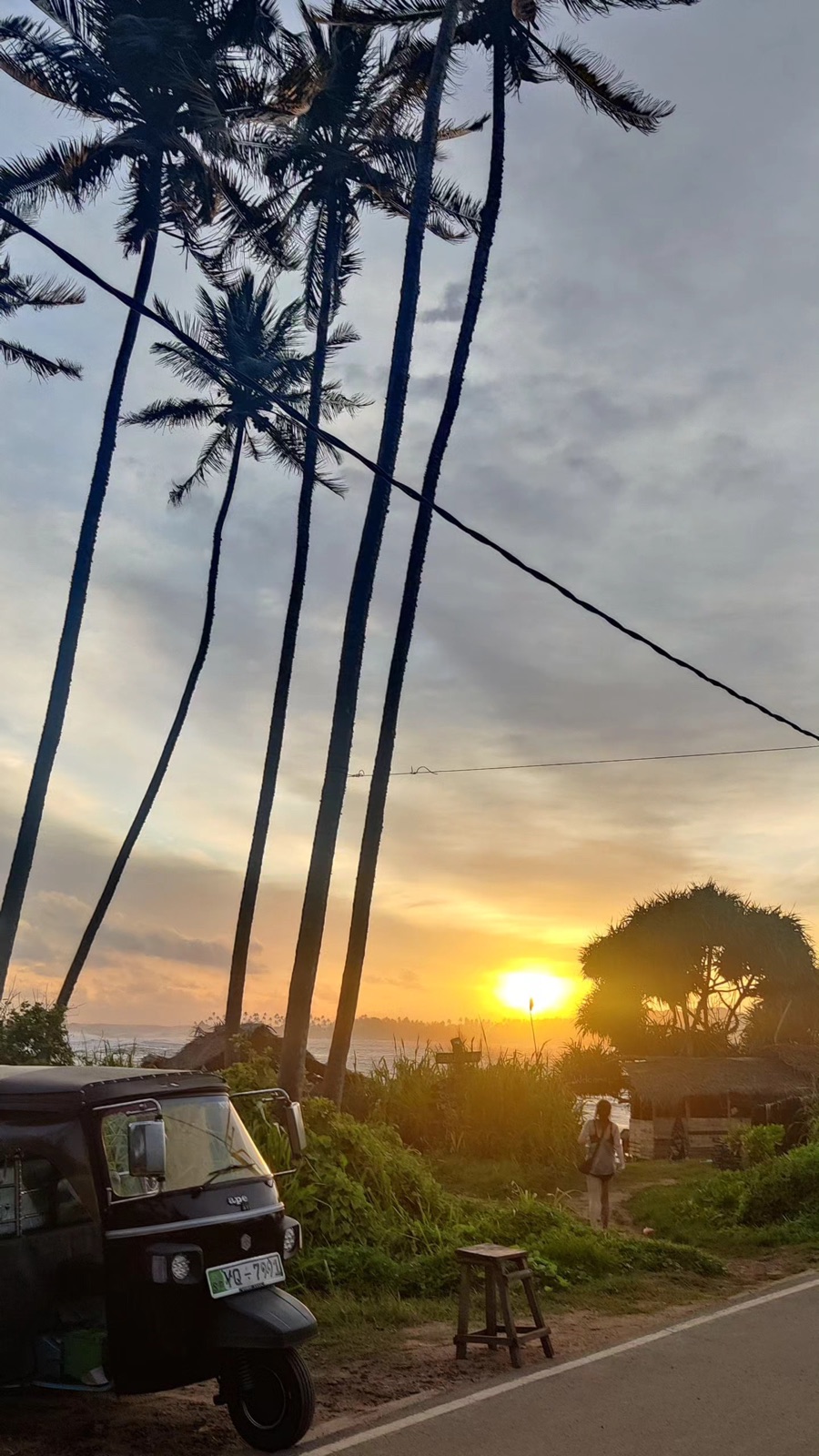 The sun setting at the end of a palm-lined road with a tuk-tuk parked on the verge, Hiriketiya