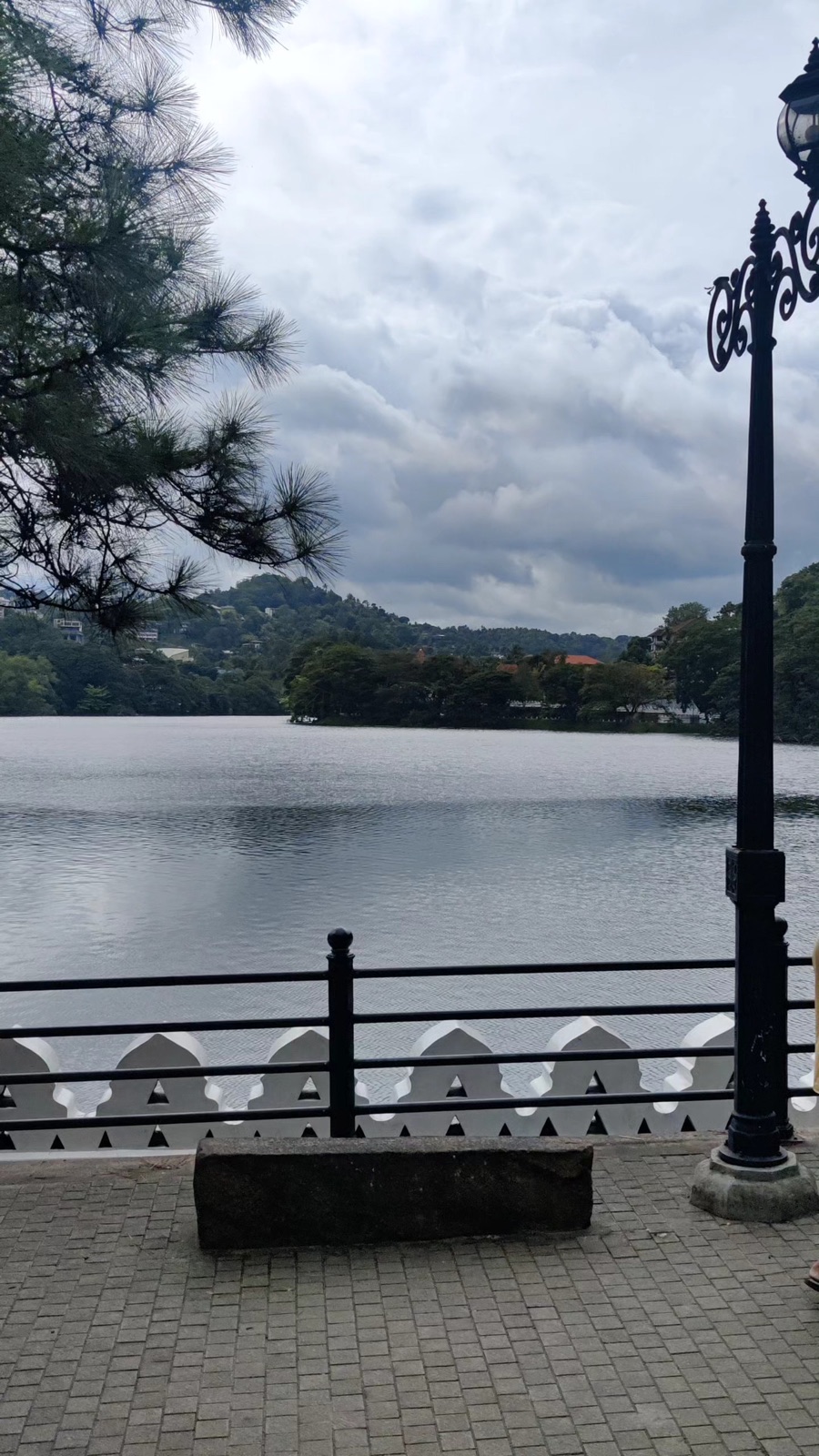 Kandy Lake with its white lace wall and lamp posts under cloudy hills