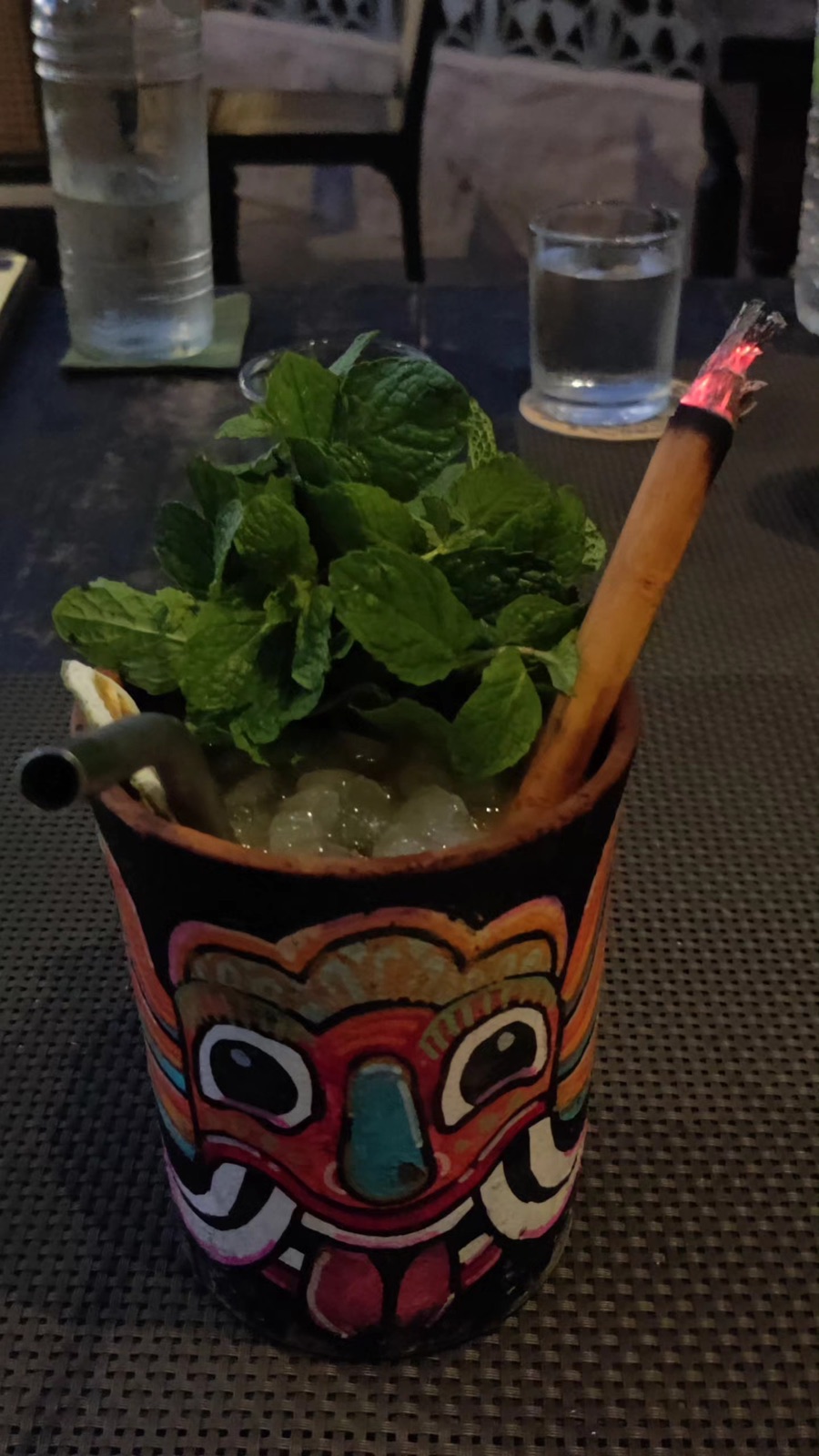 A cocktail in a Sri Lankan devil mask cup with mint and a smoking cinnamon stick at Smoke & Bitters